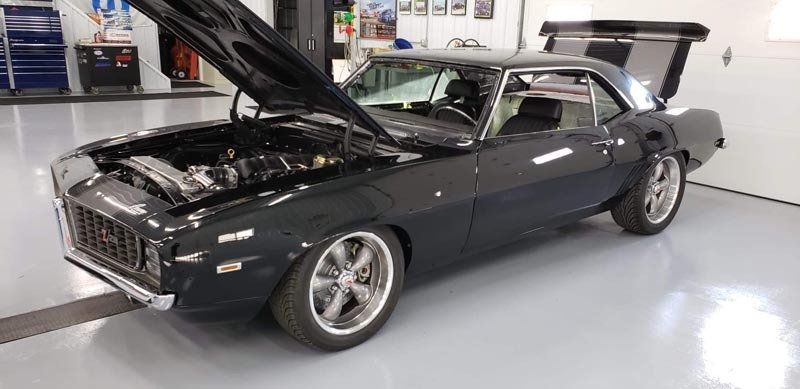A black car with the hood up is parked in a garage.