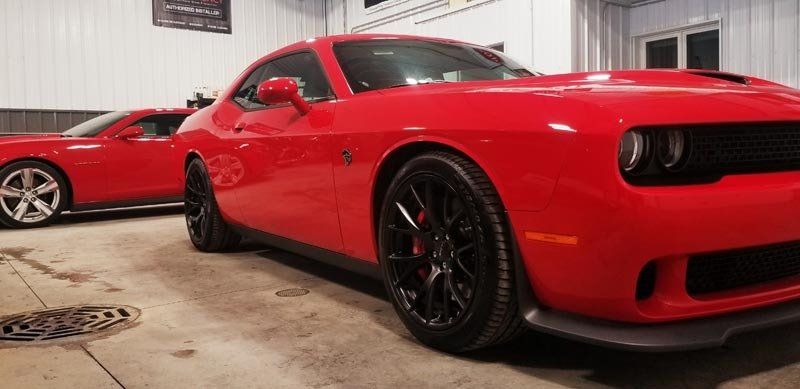 A red dodge challenger is parked in a garage next to another red car.