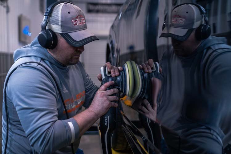 A man wearing headphones is polishing a car in a garage.