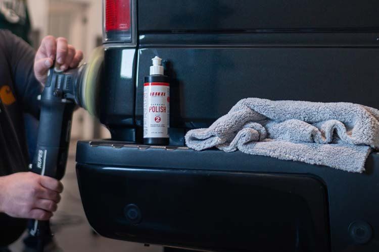 A person is polishing the back of a black truck.