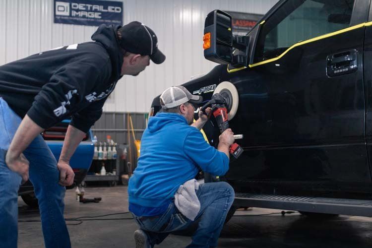 Two men are polishing a black truck in a garage.