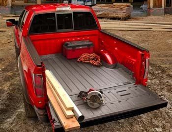 A red truck is parked on a dirt road with its bed open.