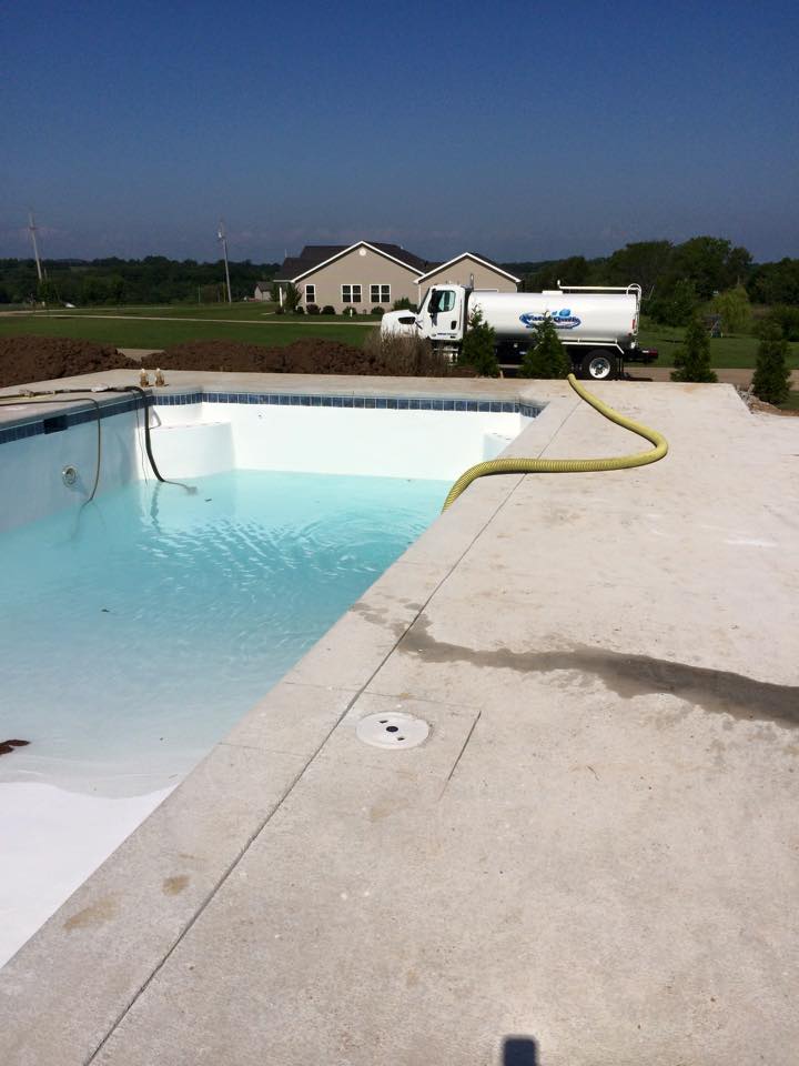 Backyard swimming pool with a hose, concrete deck, and house in the distance