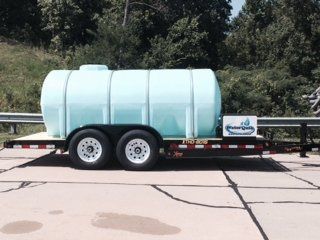 Light blue water tank trailer parked on pavement near trees