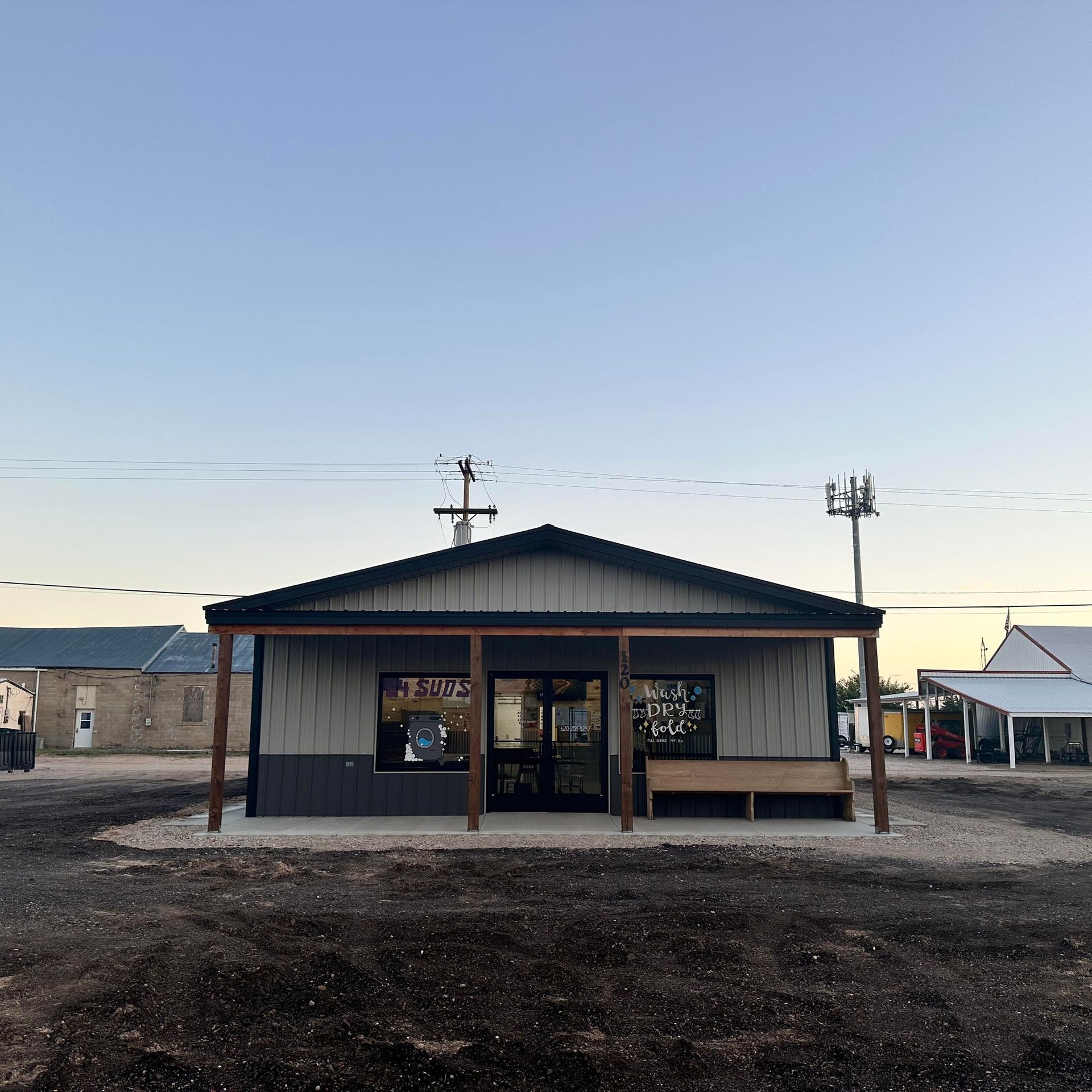 Small rustic storefront with a dark roof and wooden porch in a gravel lot at dusk