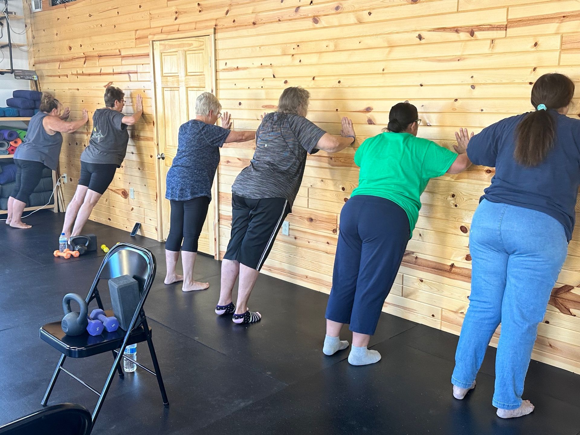 People exercising with pushups against a wooden wall in a studio, with a kettlebell chair in front