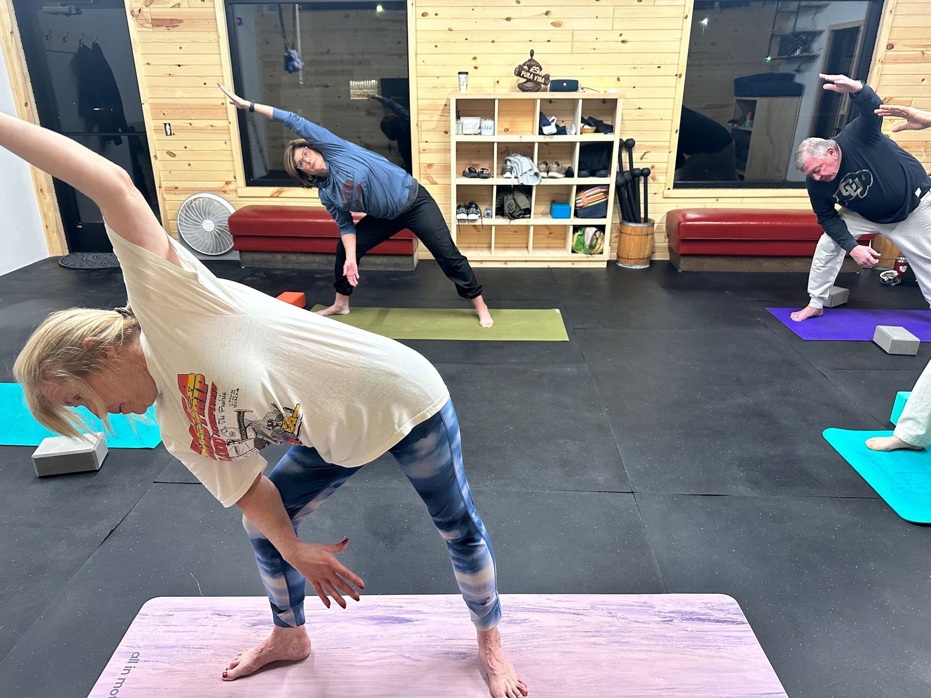 People doing yoga stretches on mats in a studio with black flooring and wooden walls.