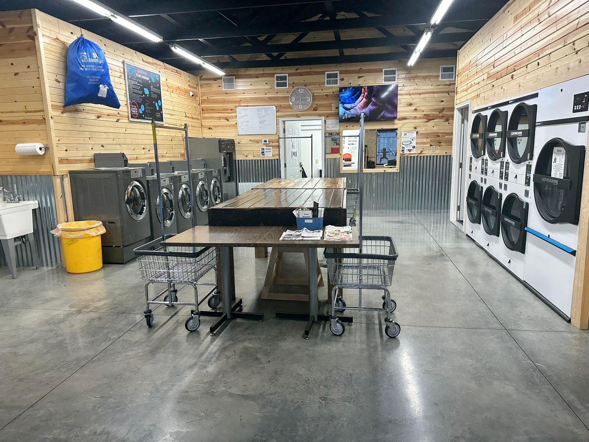 Woodworking shop with tables, tools, metal racks, and wall-mounted fans in a large workshop.