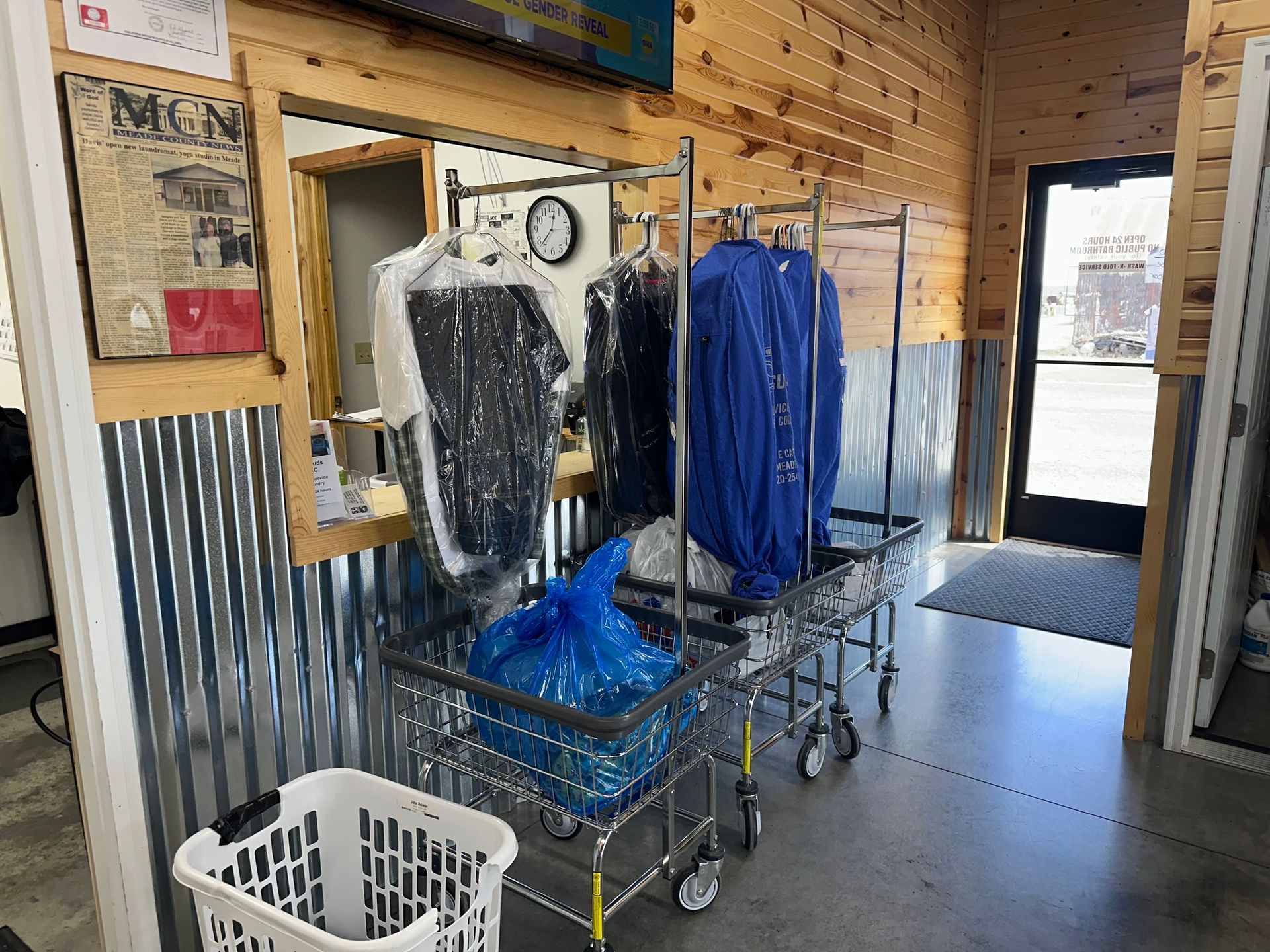 Clothing rack with hanging garments and laundry baskets in a small industrial laundry room