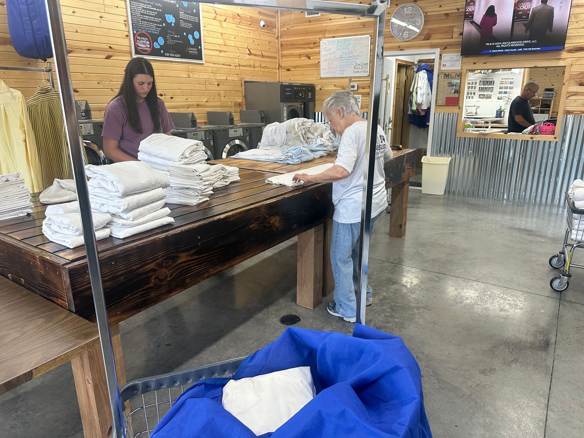 Retail store checkout counter with two employees folding white towels and a blue bin in the foreground