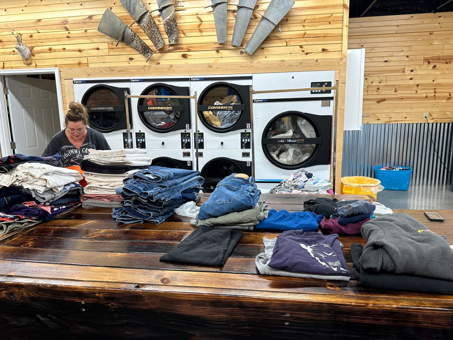 Laundry shop with a person folding clothes beside stacked jeans and front-loading machines