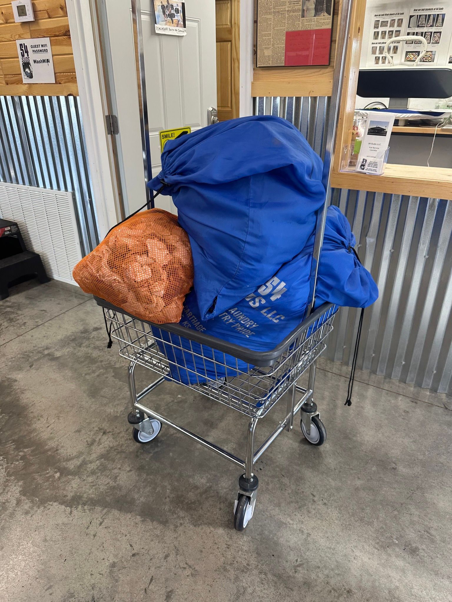 Blue backpack and orange sleeping bag on a wire shopping cart in an indoor facility.