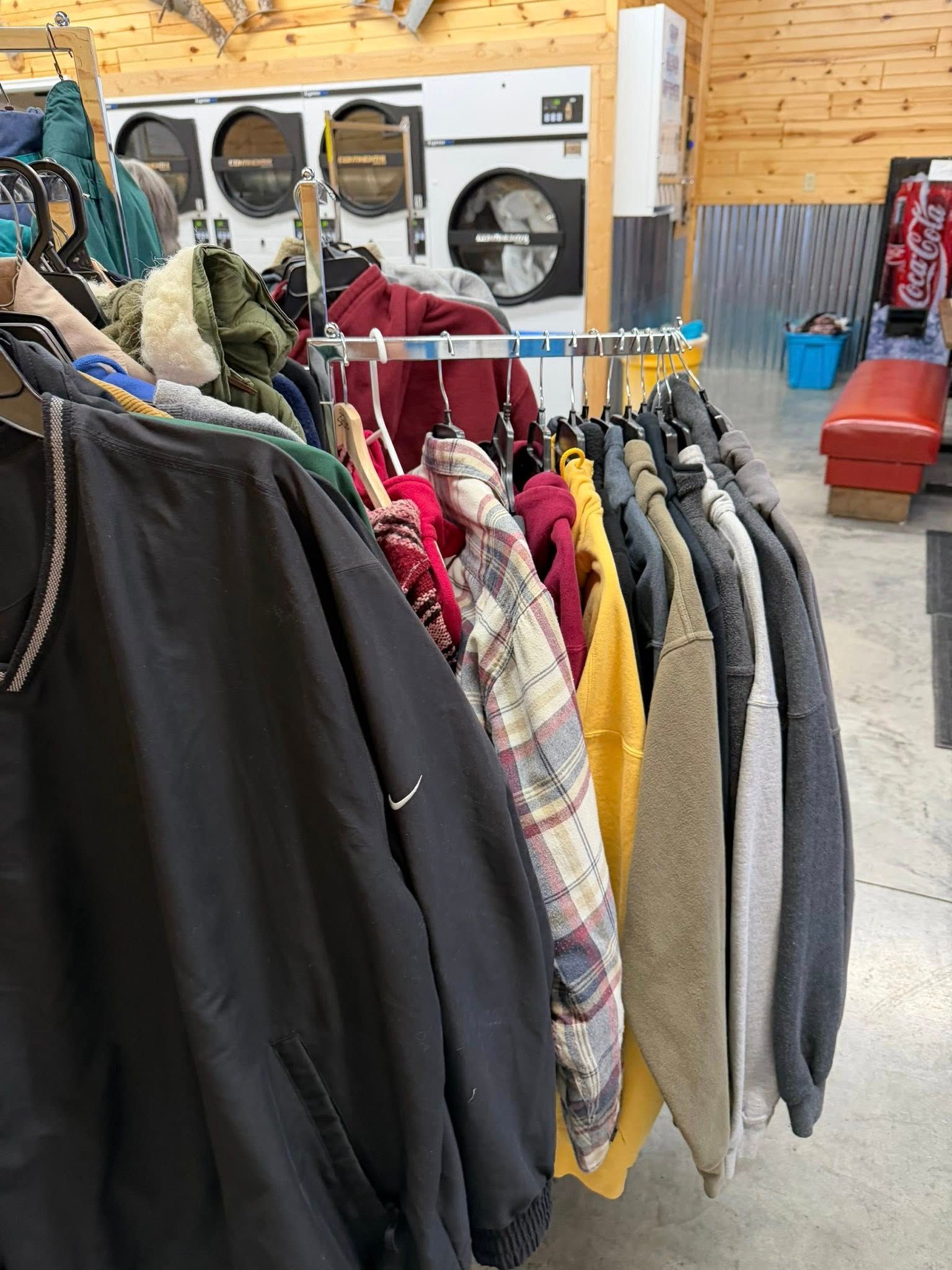 Coats and jackets hanging on a rack outside a laundromat with washers visible in the background