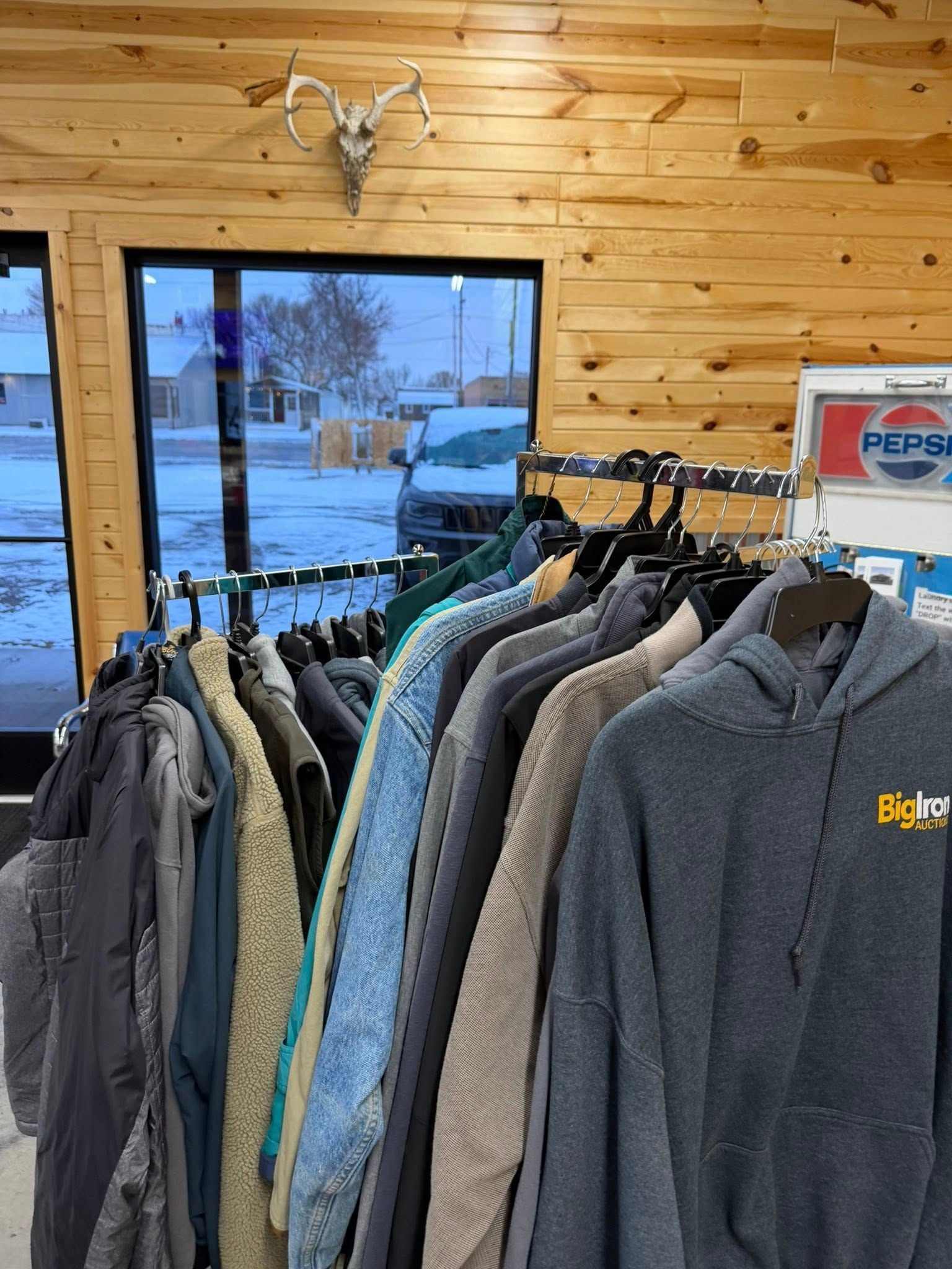Clothing rack with coats and sweaters in a rustic shop by a window and wooden wall.
