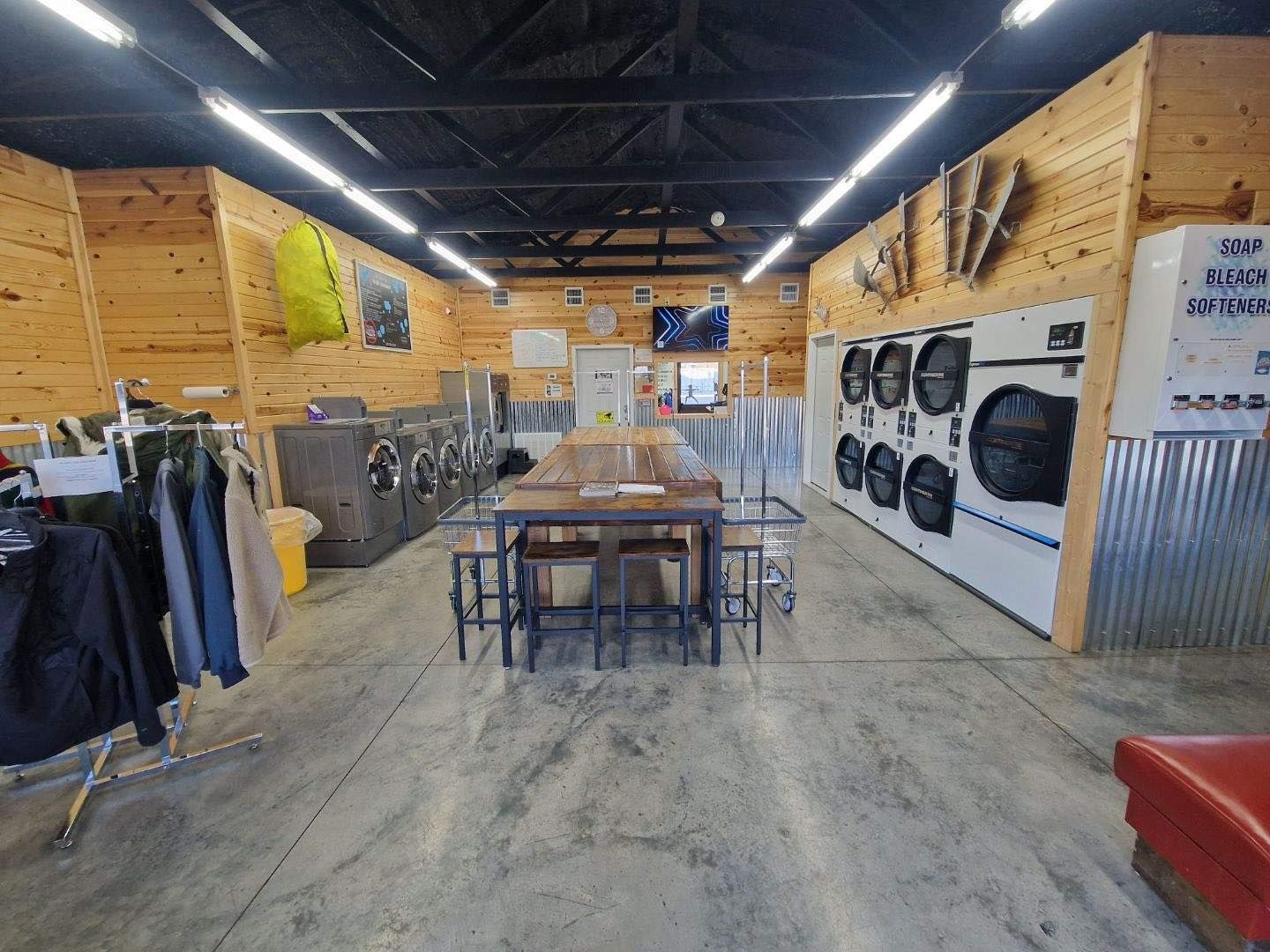 Laundry room with rows of washers and dryers, folding table, clothes racks, and wood-paneled walls