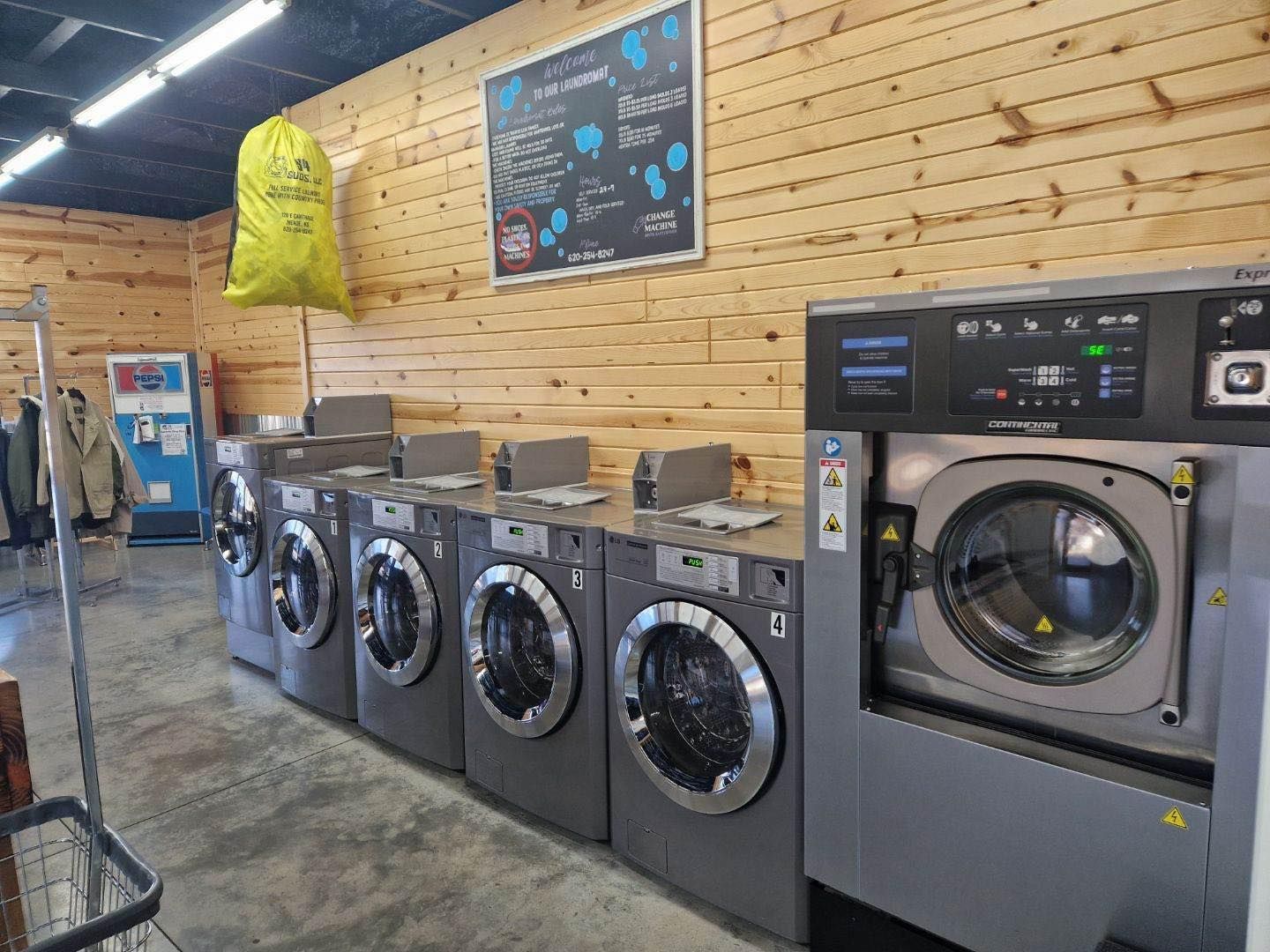 Laundry room with row of gray front-loading machines against a wooden wall