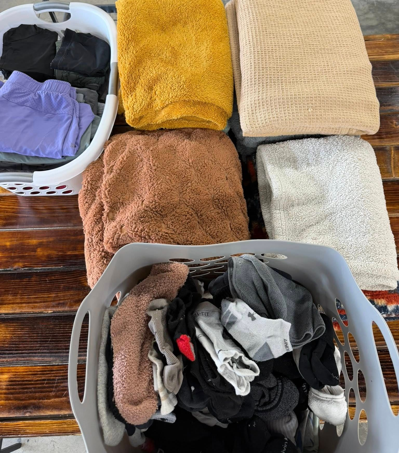 Folded towels and clothes in two laundry baskets on a wooden surface.
