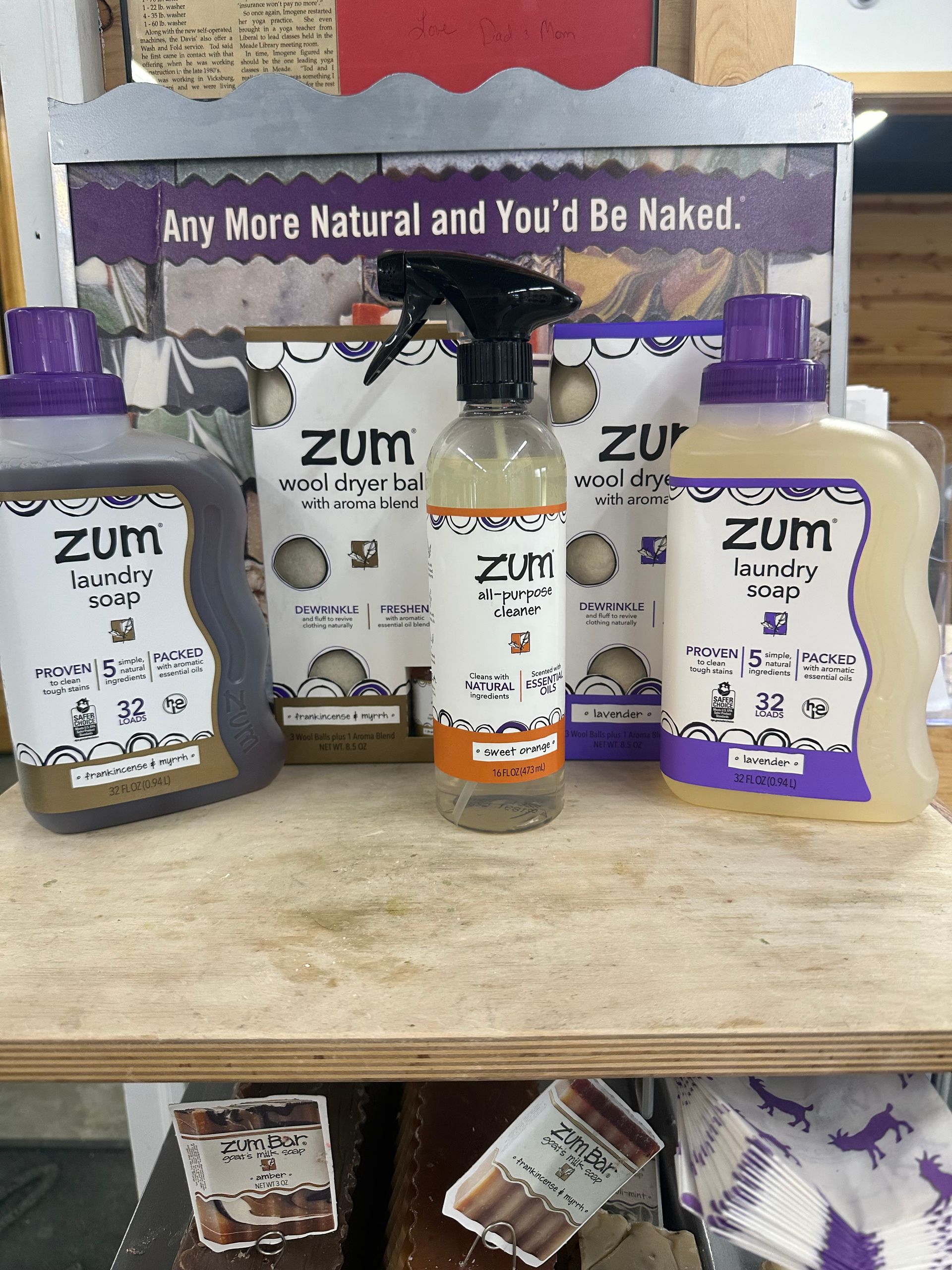Assorted Zum natural soap and lotion bottles on a shelf with a sign reading “Any More Natural and You’ll Be Naked.”