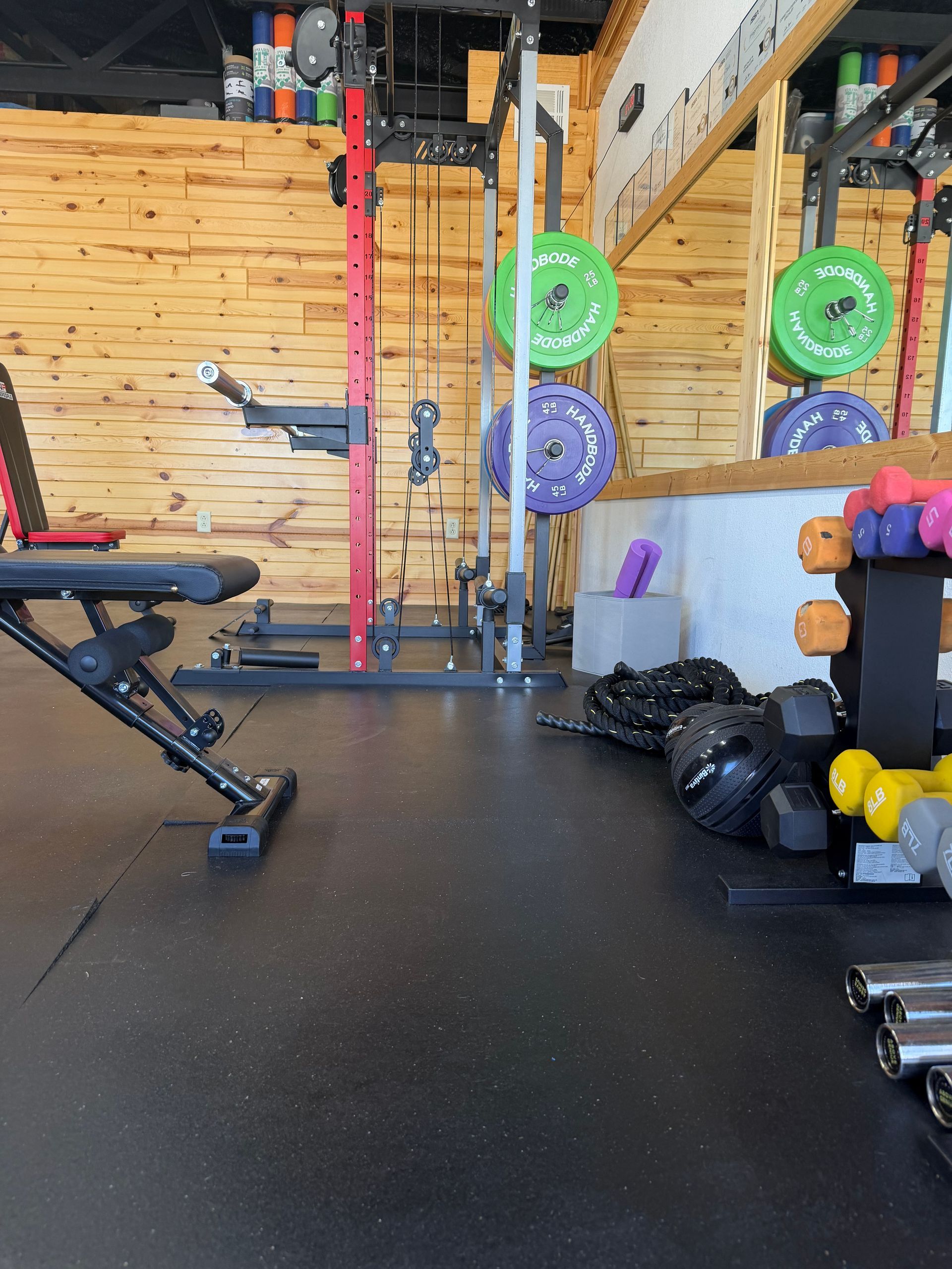 Home gym with squat rack, bench, dumbbells, and weight plates on black flooring