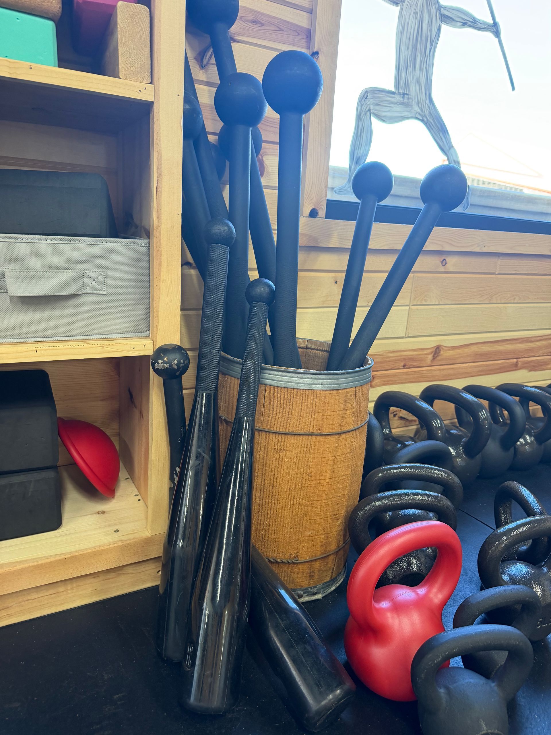Workout equipment stored in a corner, including kettlebells and weighted clubs in a woven basket.