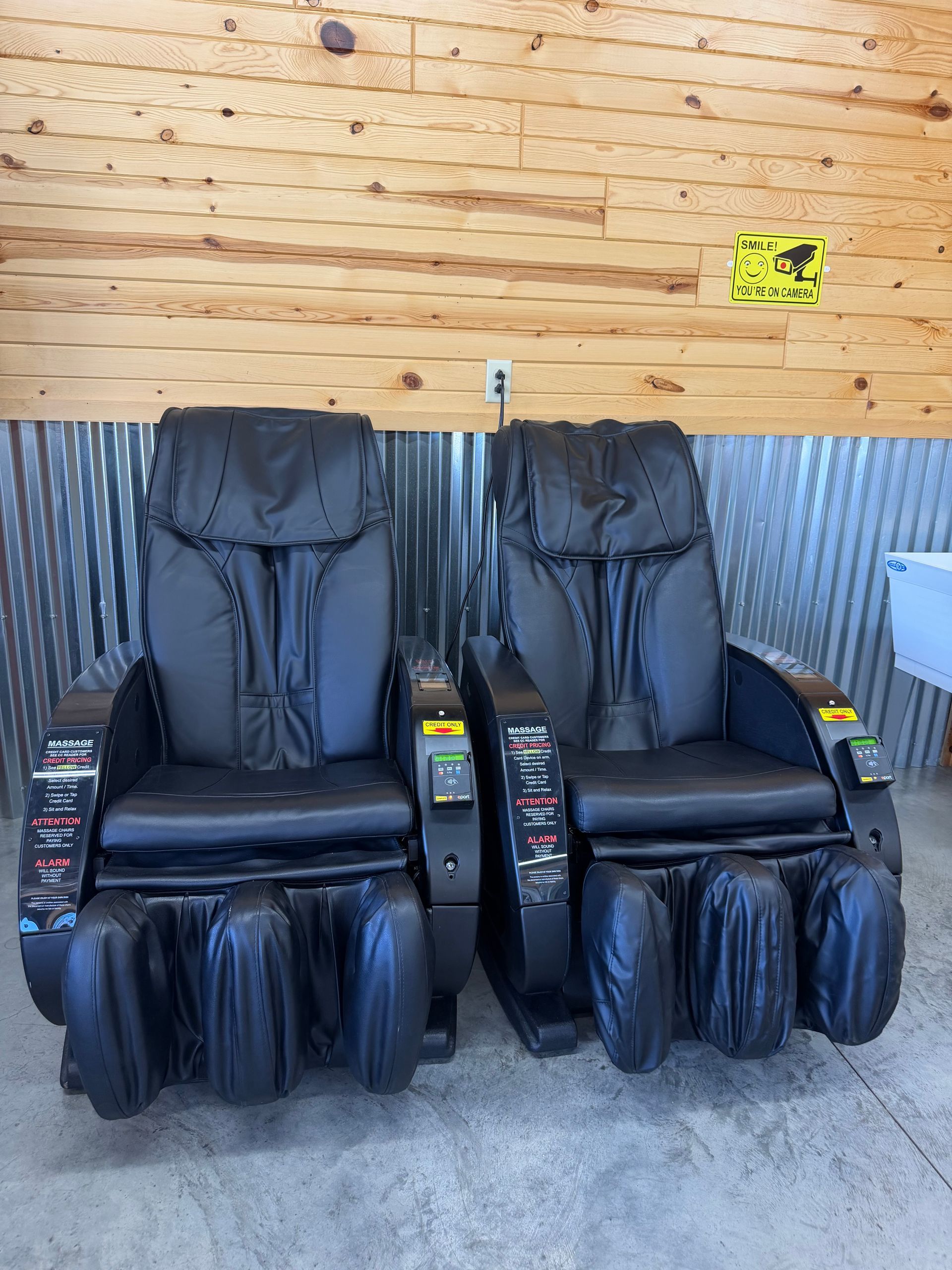 Two black massage chairs against a wooden wall in a waiting area