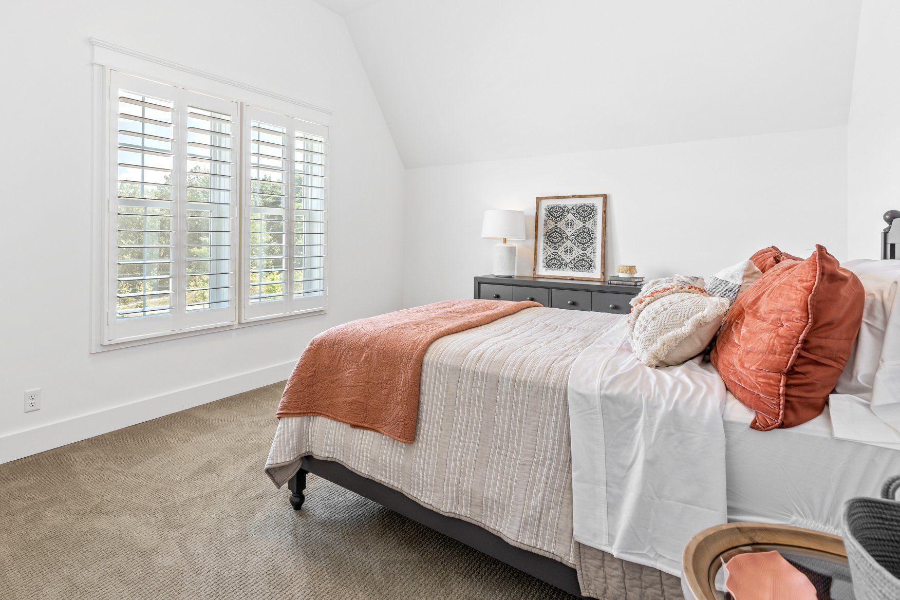 Bright bedroom with a bed, coral pillows, and a dresser under a sloped white ceiling