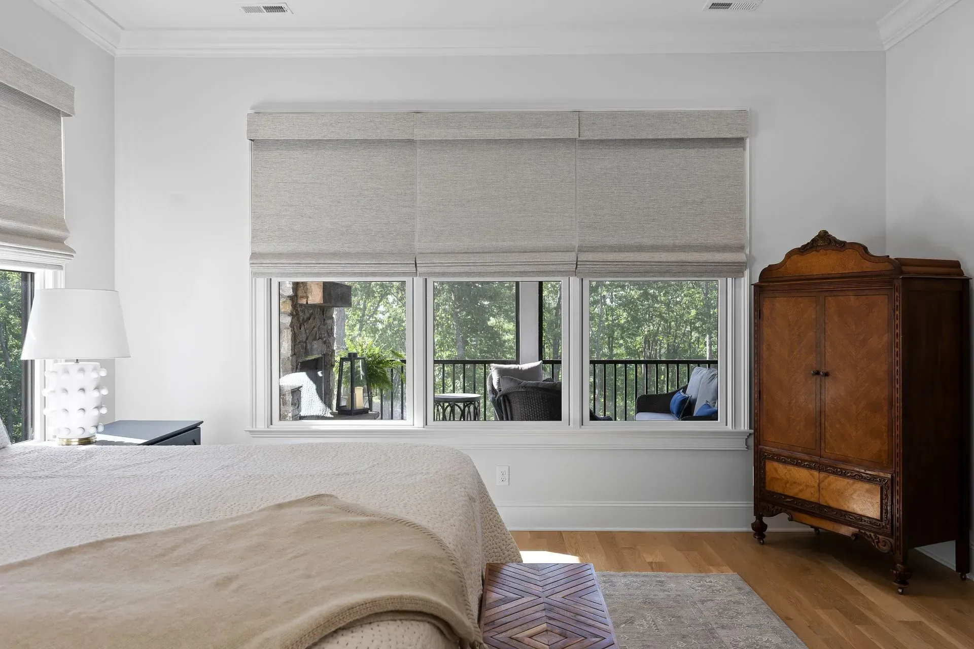 Bright bedroom with a window seat, gray blinds, white bed, and wooden armoire on hardwood floors