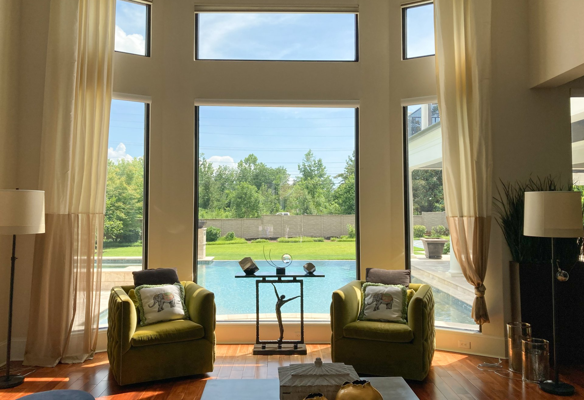 A living room with two green chairs and a large window overlooking a swimming pool.