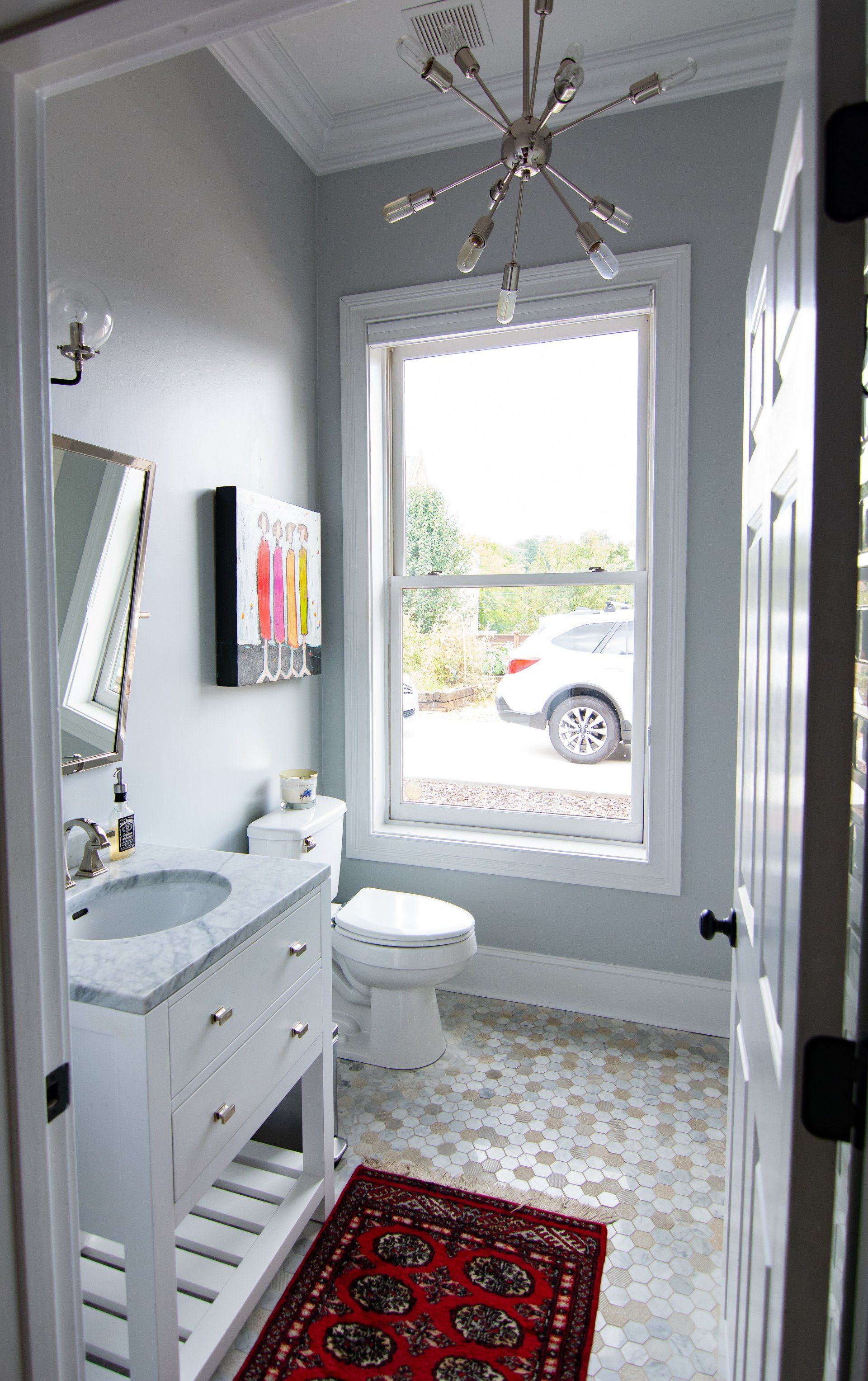 A bathroom with a toilet , sink , mirror and window.