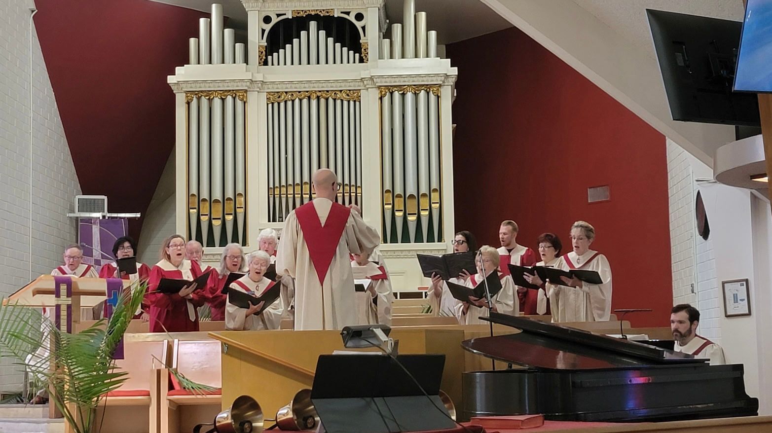 Church choir performing in front of a large pipe organ, with a piano in the foreground Church choir performing in front of a large pipe organ, with a piano in the foreground