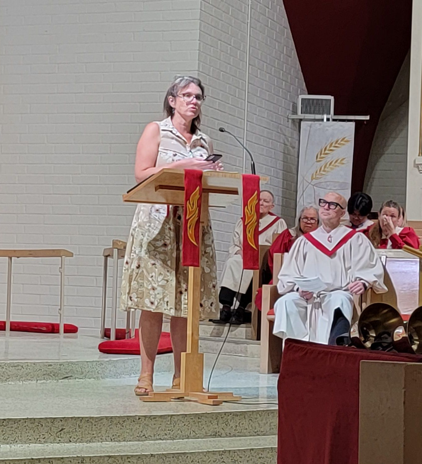 Speaker at a lectern during a church service, with choir seated behind her. Speaker at a lectern during a church service, with choir seated behind her.