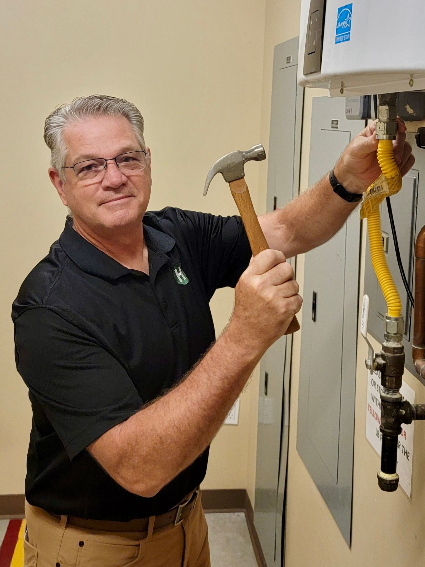 Man in black shirt using a hammer on an open electrical panel in a utility room Man in black shirt using a hammer on an open electrical panel in a utility room
