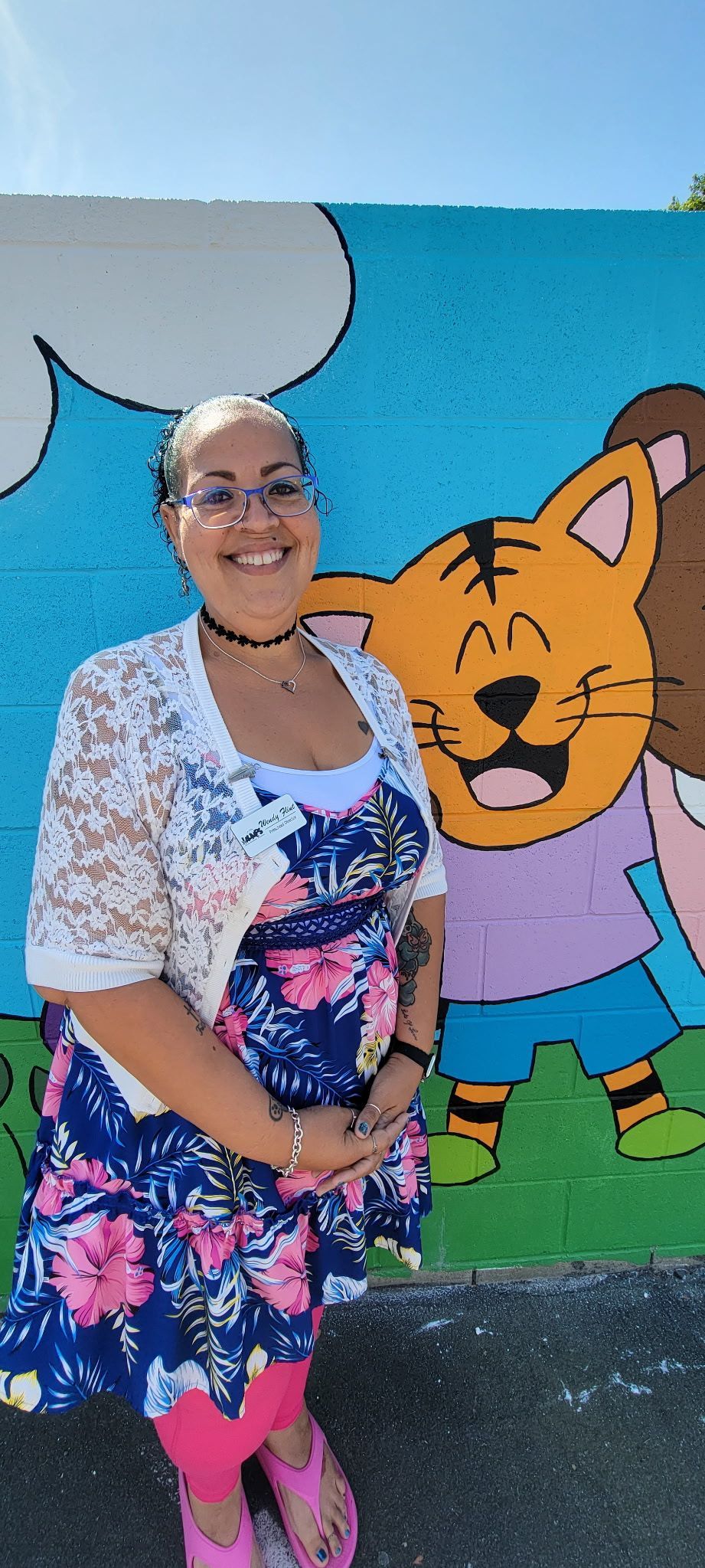 Woman posing beside a colorful cartoon cat mural outdoors.