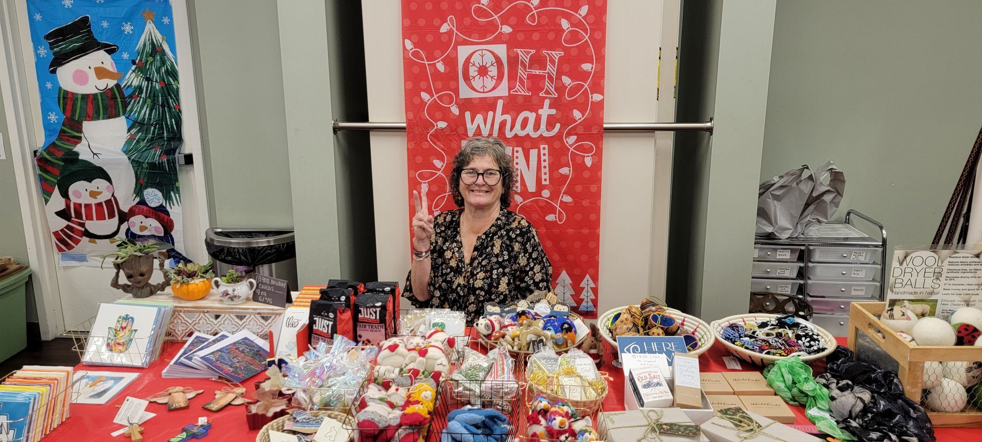 Woman at a market table with holiday crafts, gifts, and decorations displayed on red tablecloths Woman at a market table with holiday crafts, gifts, and decorations displayed on red tablecloths