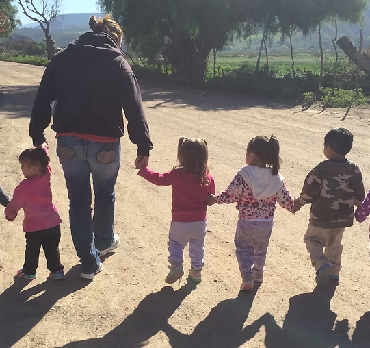 Adult and four children holding hands, walking along a sunlit dirt path outdoors. Adult and four children holding hands, walking along a sunlit dirt path outdoors.
