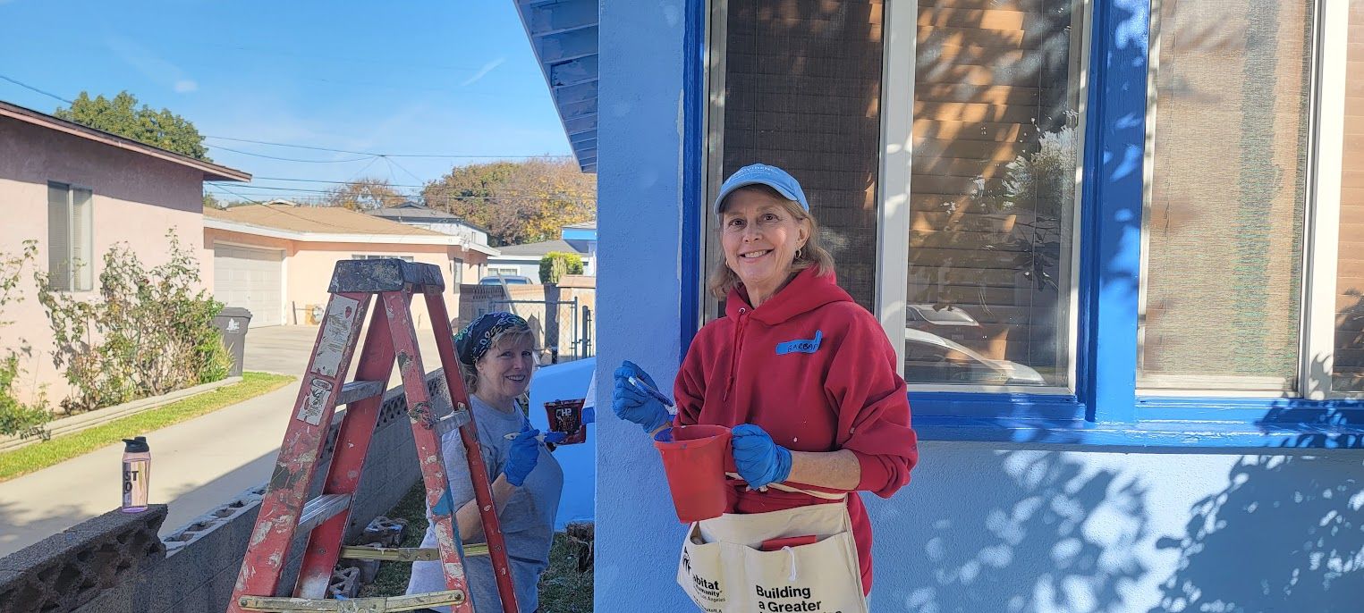 Person in red jacket and cap stands by a ladder painting a blue house exterior. Person in red jacket and cap stands by a ladder painting a blue house exterior.