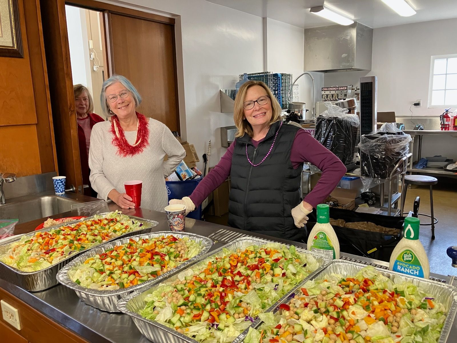 Two women serving colorful pasta salads at a buffet table in a kitchen. Two women serving colorful pasta salads at a buffet table in a kitchen.