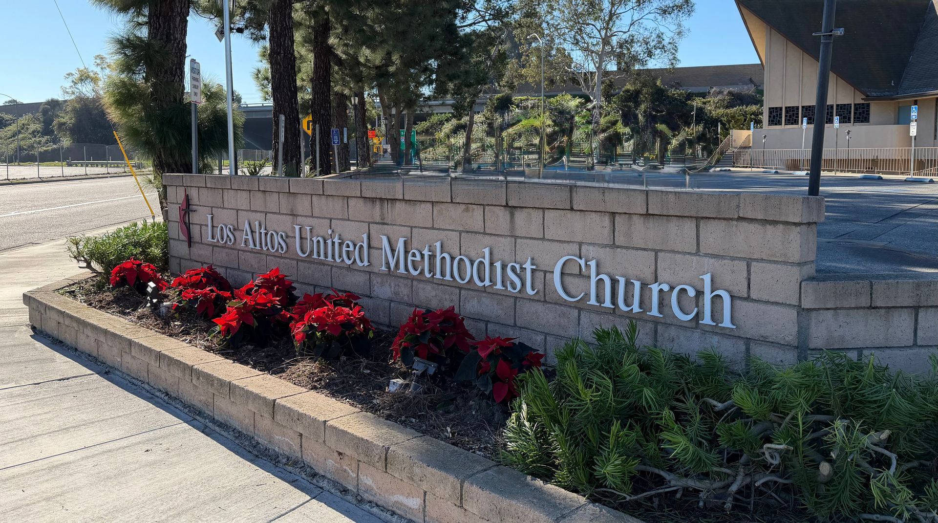 Stone sign for United Methodist Church with red flowers and greenery along the base