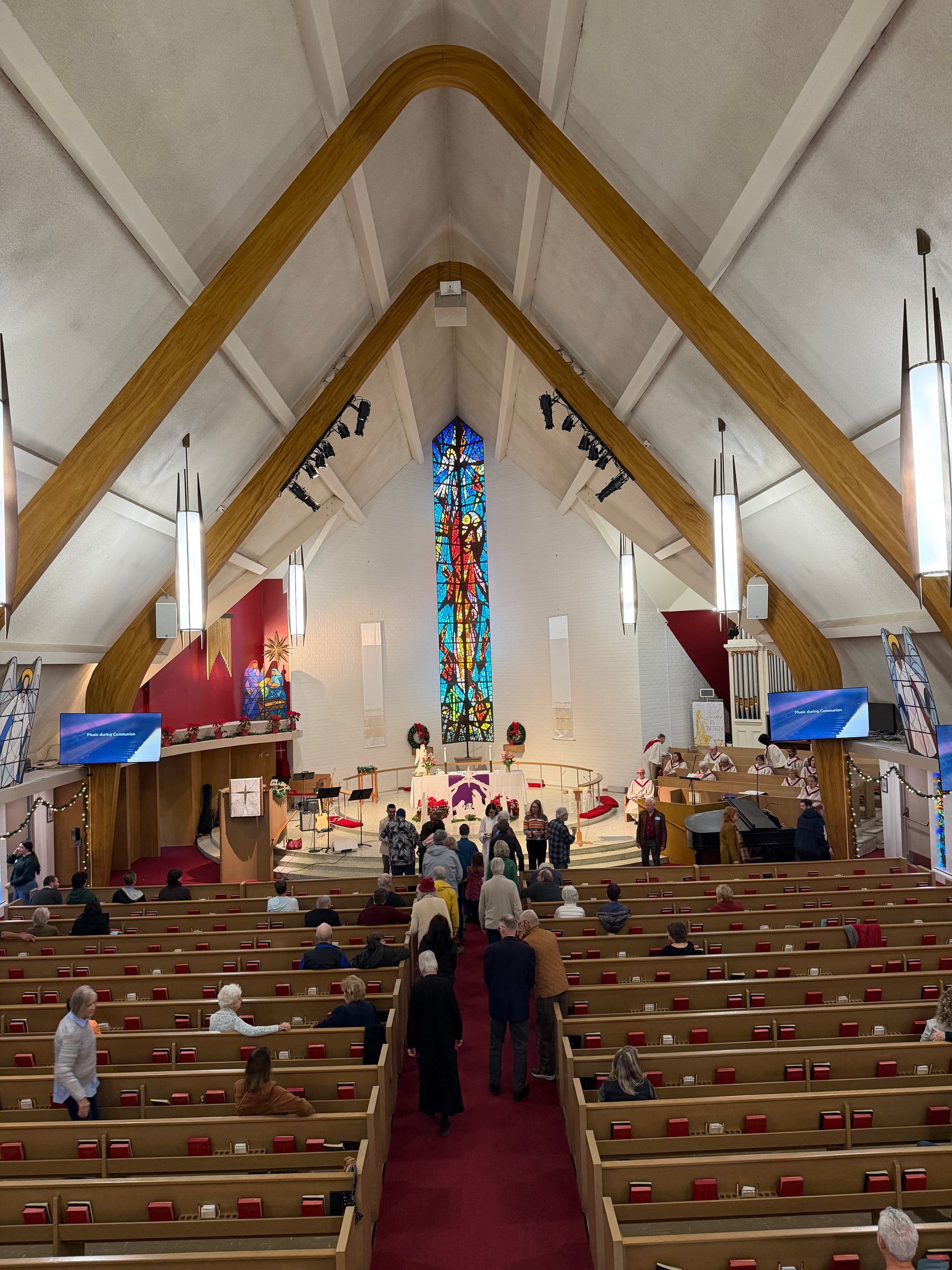 Church sanctuary with wooden beams, stained-glass window, pews, and people gathered near the altar