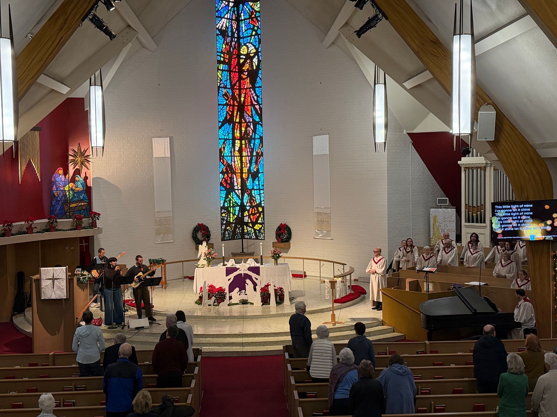 Church sanctuary with choir and musicians performing near a colorful stained-glass window