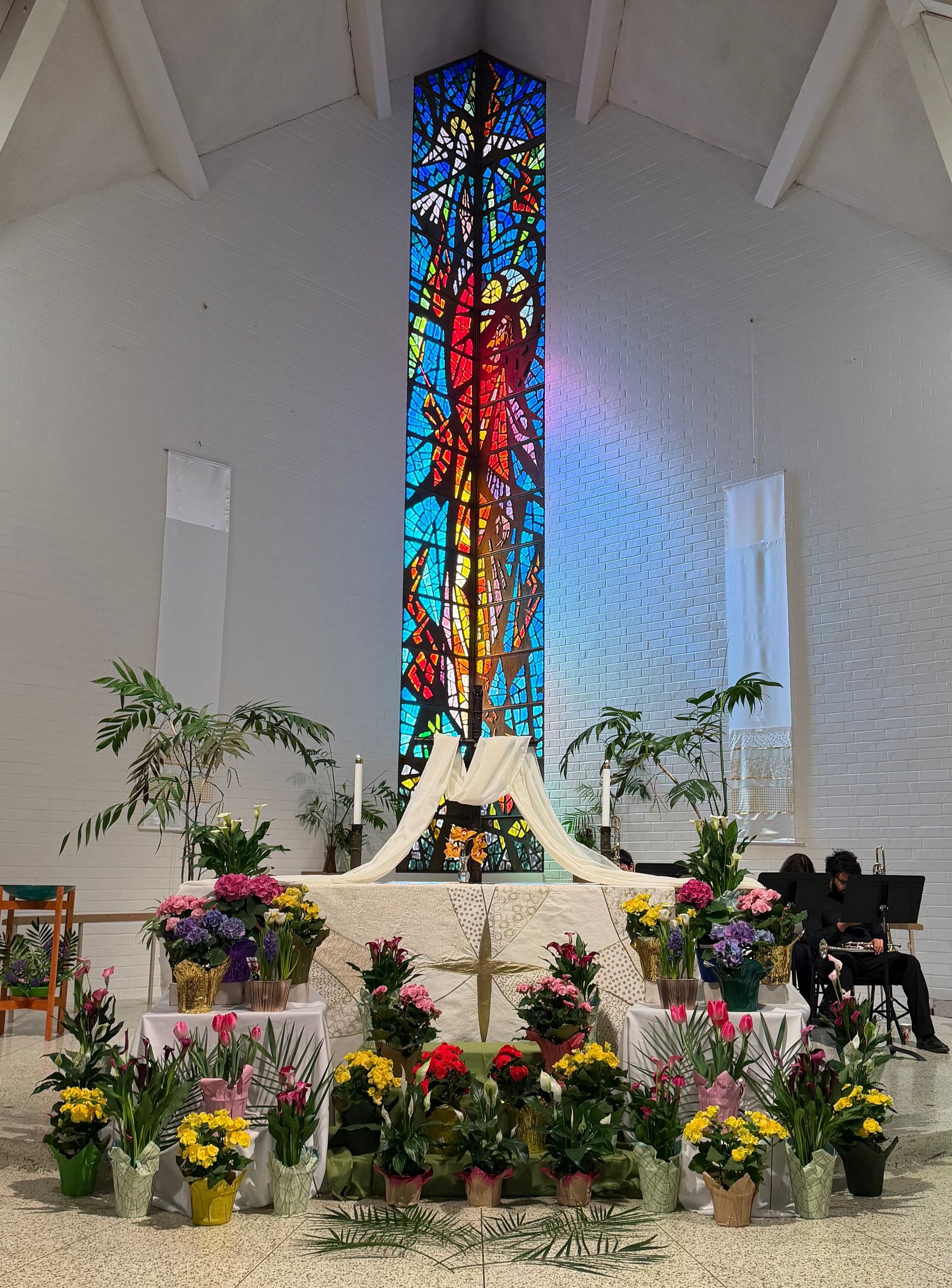 Church altar decorated with colorful flowers and a tall stained-glass window behind it Church altar decorated with colorful flowers and a tall stained-glass window behind it