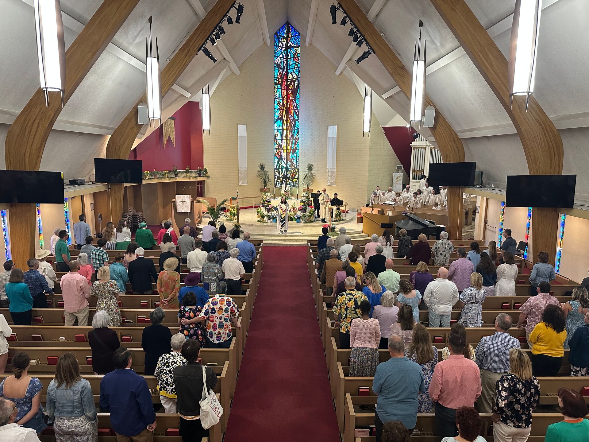 Congregation in a church sanctuary with a red aisle and stained-glass window at the front