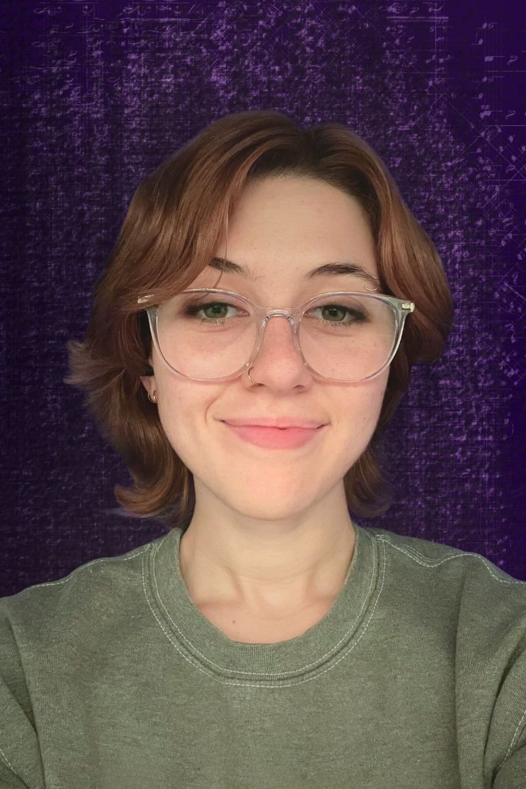 Person with glasses and short brown hair smiling against a purple patterned background.