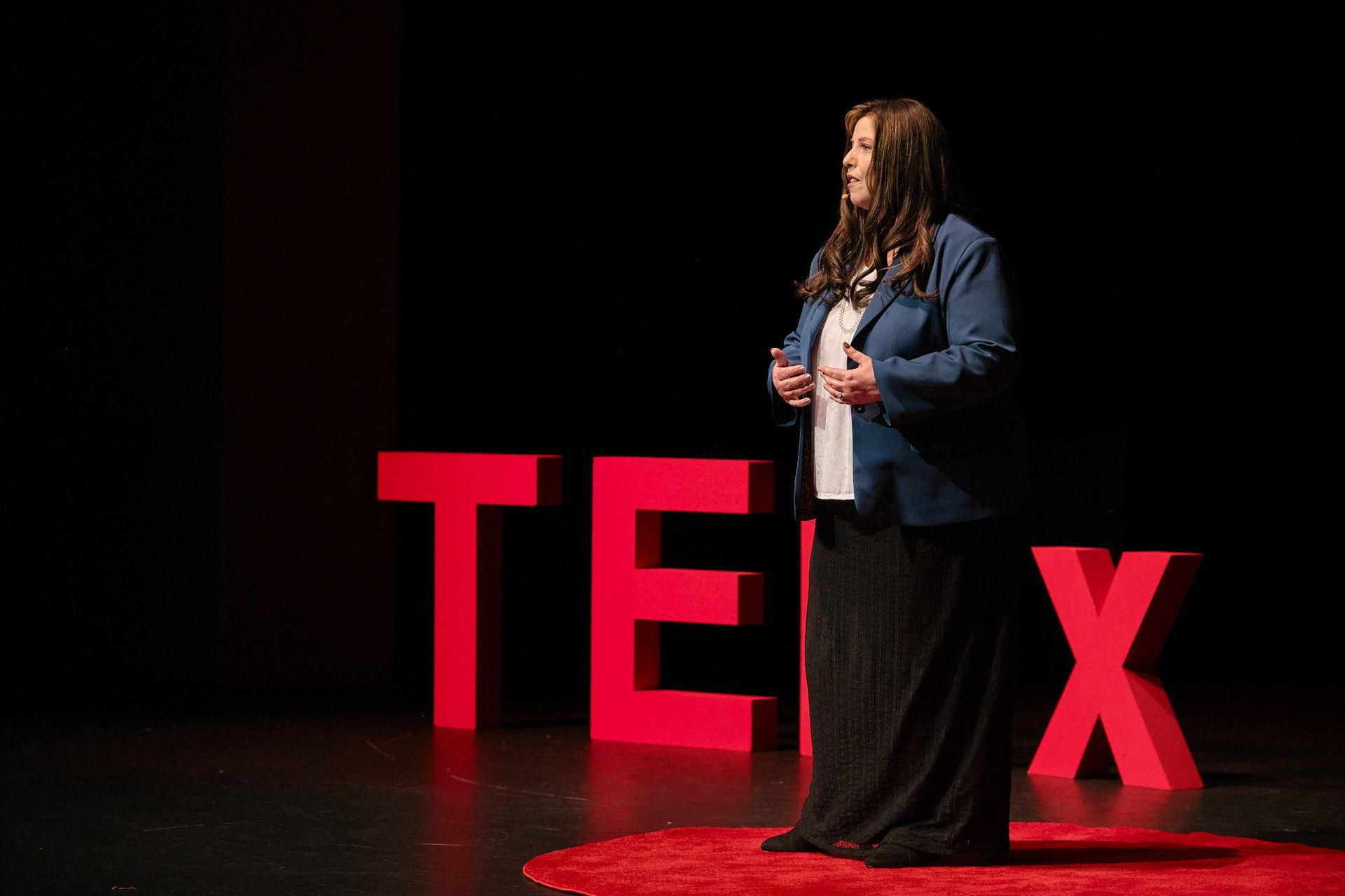A presenter stands on a stage in front of large, red