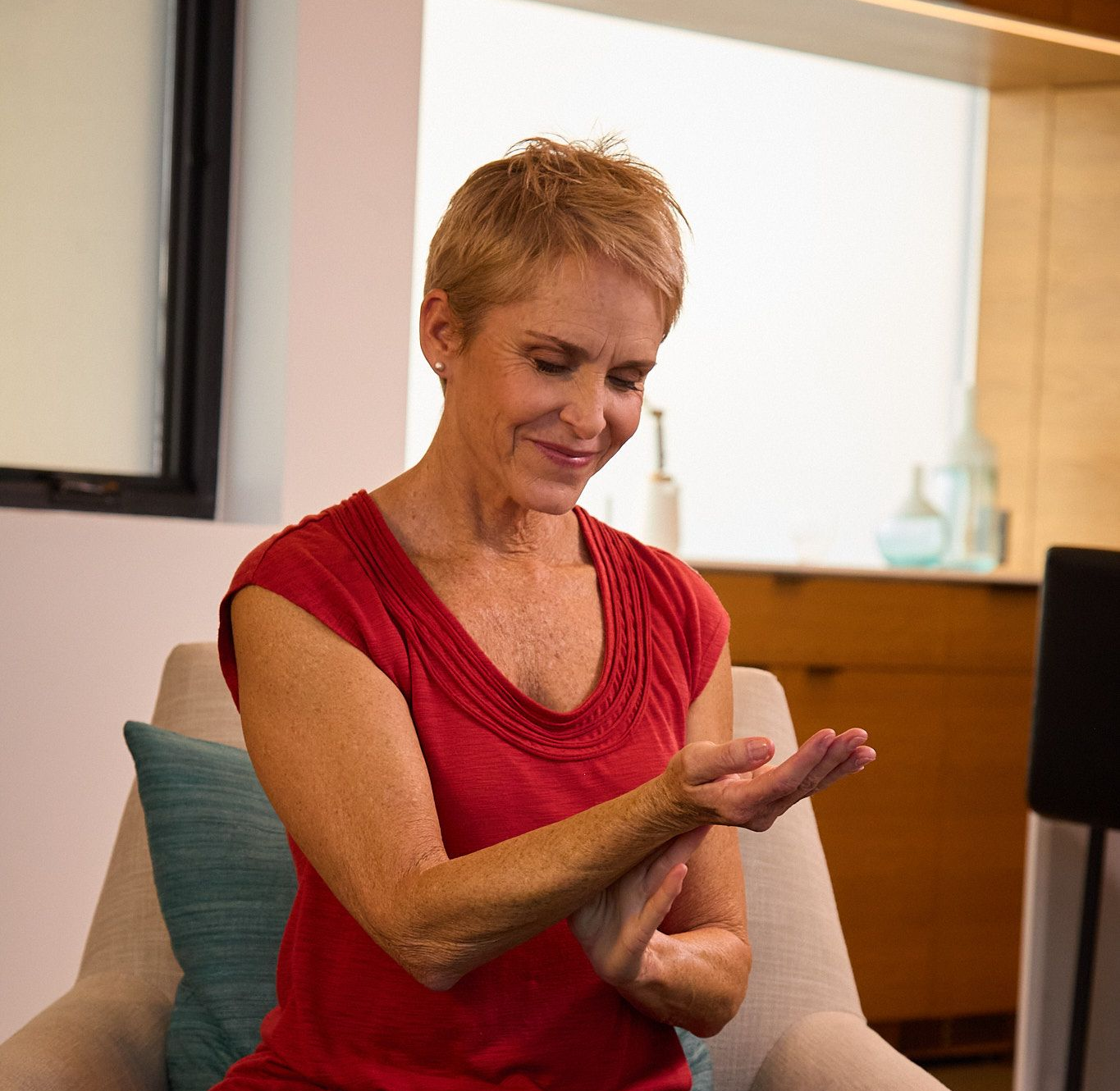 A person wearing a red top sits in a chair, holding their hands out and looking down at their palms.