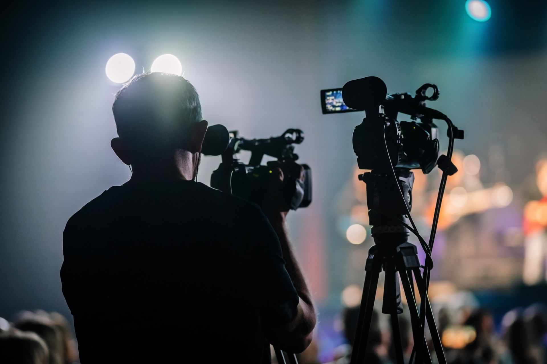 Videographer filming an event from behind the camera on a tripod.