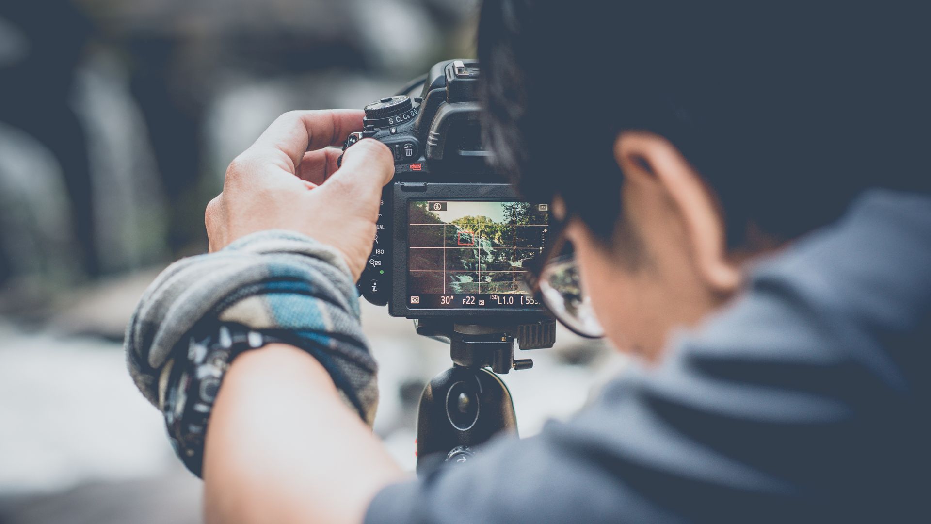 Person adjusting camera on a tripod, viewing a scene on the screen.
