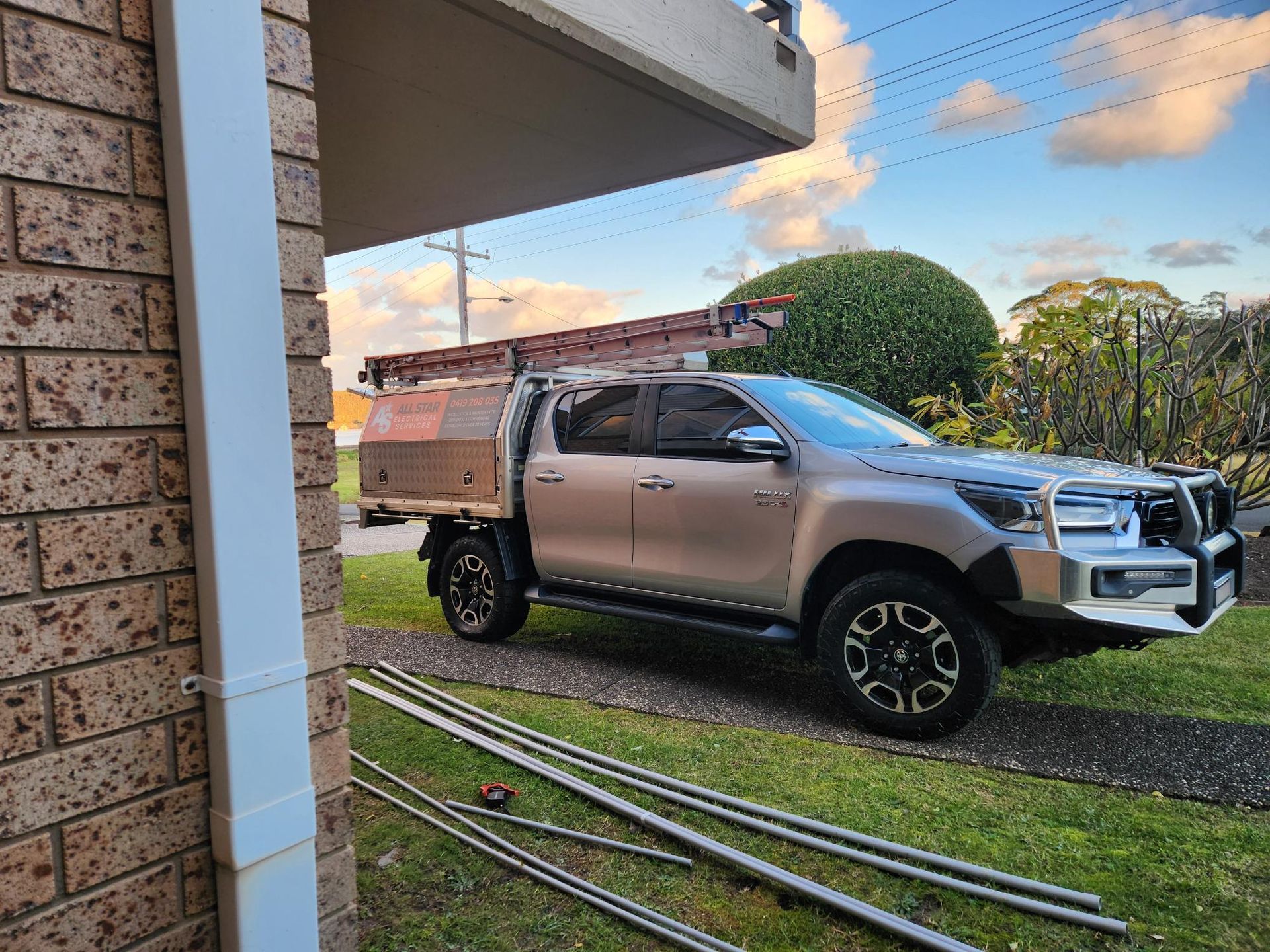 A silver pickup truck parked on a driveway with gutter materials and a ladder, near a brick house.