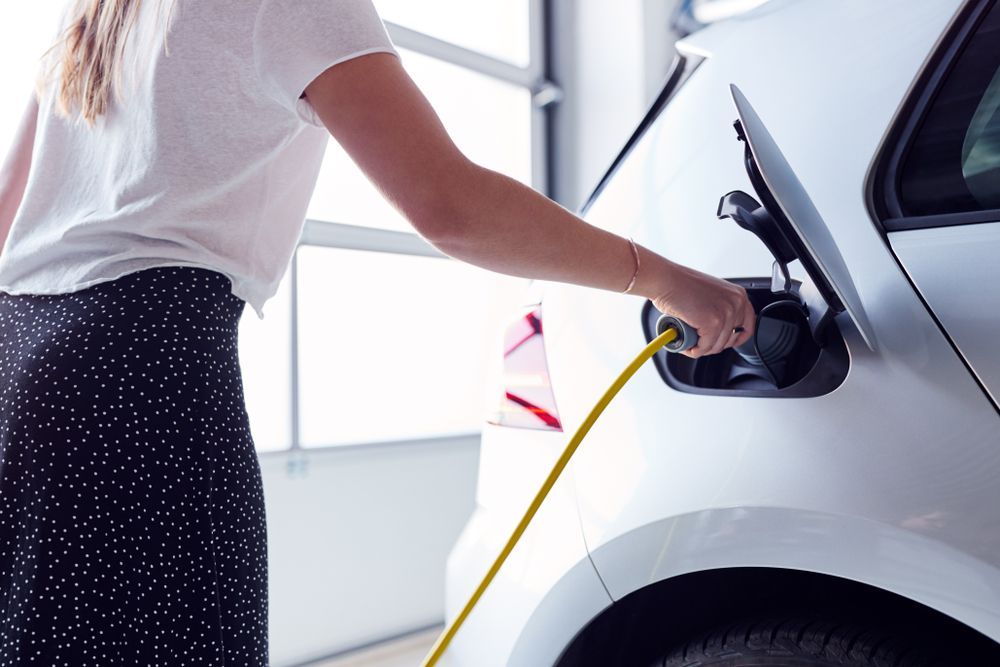 A Woman Is Charging Her Electric Car in A Garage — All Star Electrical Services in Horsley, NSW