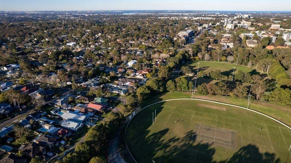 Aerial view of a suburban neighborhood beside a green sports field under clear skies. — All Star Electrical Services in Sutherland Shire, NSW